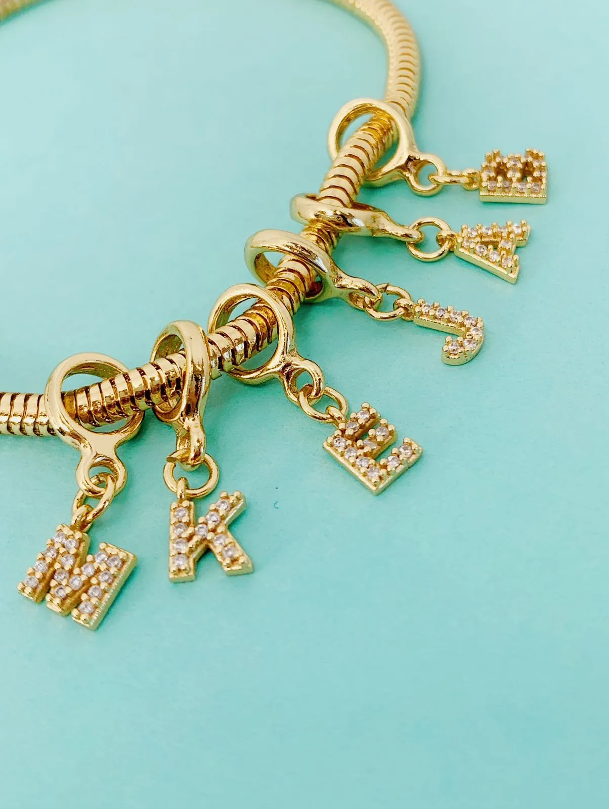 BERLOQUE DE LETRA M CRAVEJADO. BANHADO A OURO 18K.